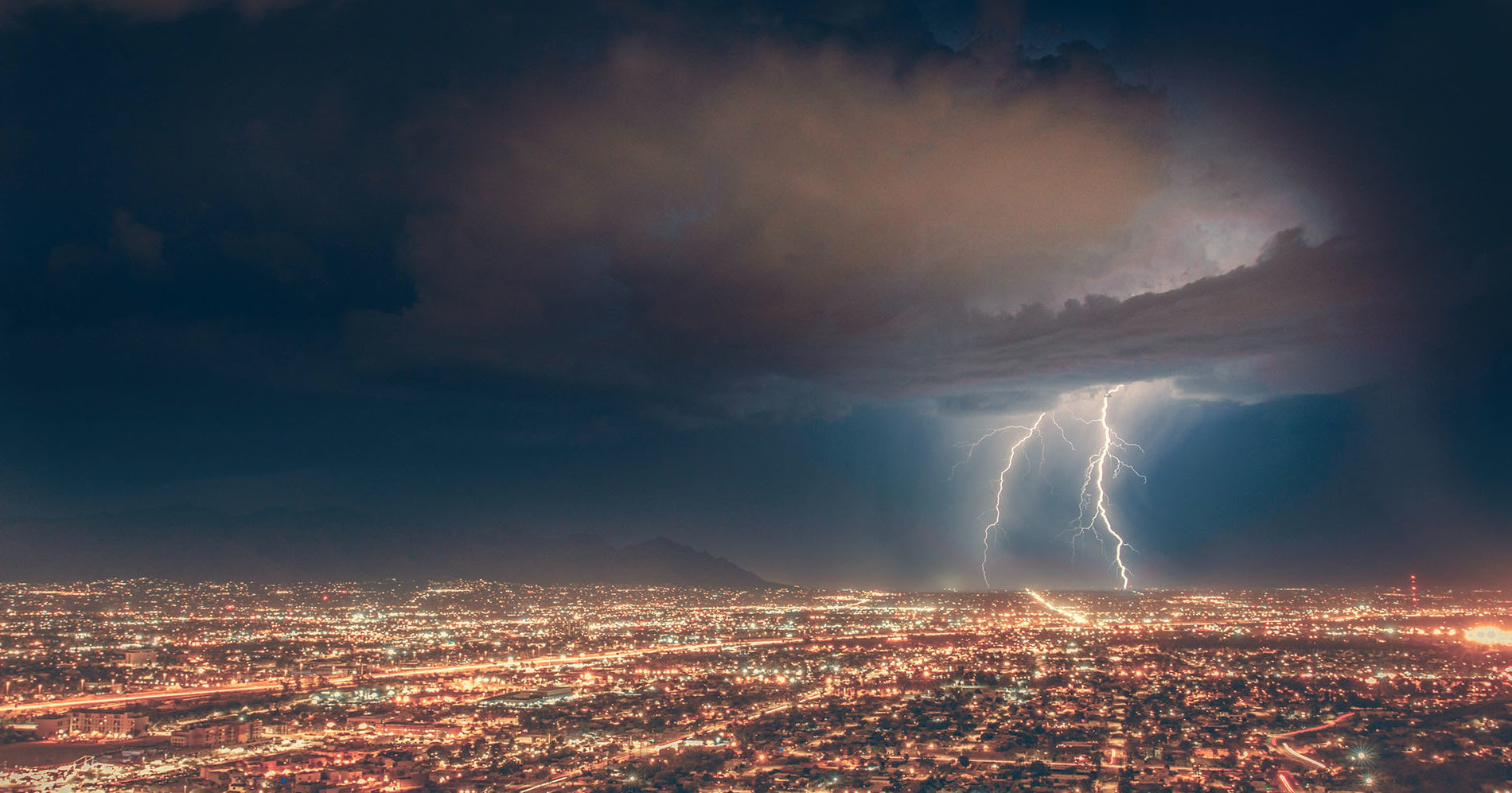 Lightning striking the ground at the edge of a large city.
