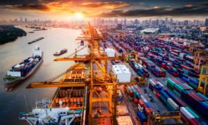 A city on a river with many barges filled with shipping containers.